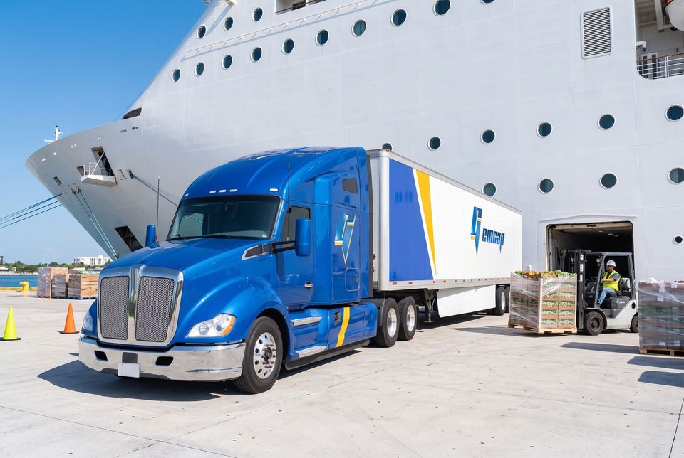 A blue GEMCAP tractor-trailer at the cruise pier while a forklift carries pallets of fresh produce into the ship